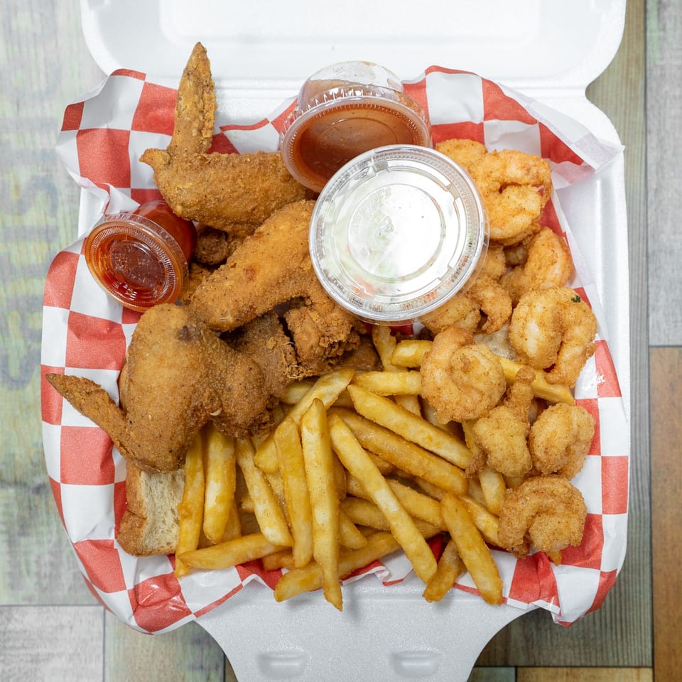 Fried chicken wings, shrimp, and french fries with dipping sauces in a styrofoam container.