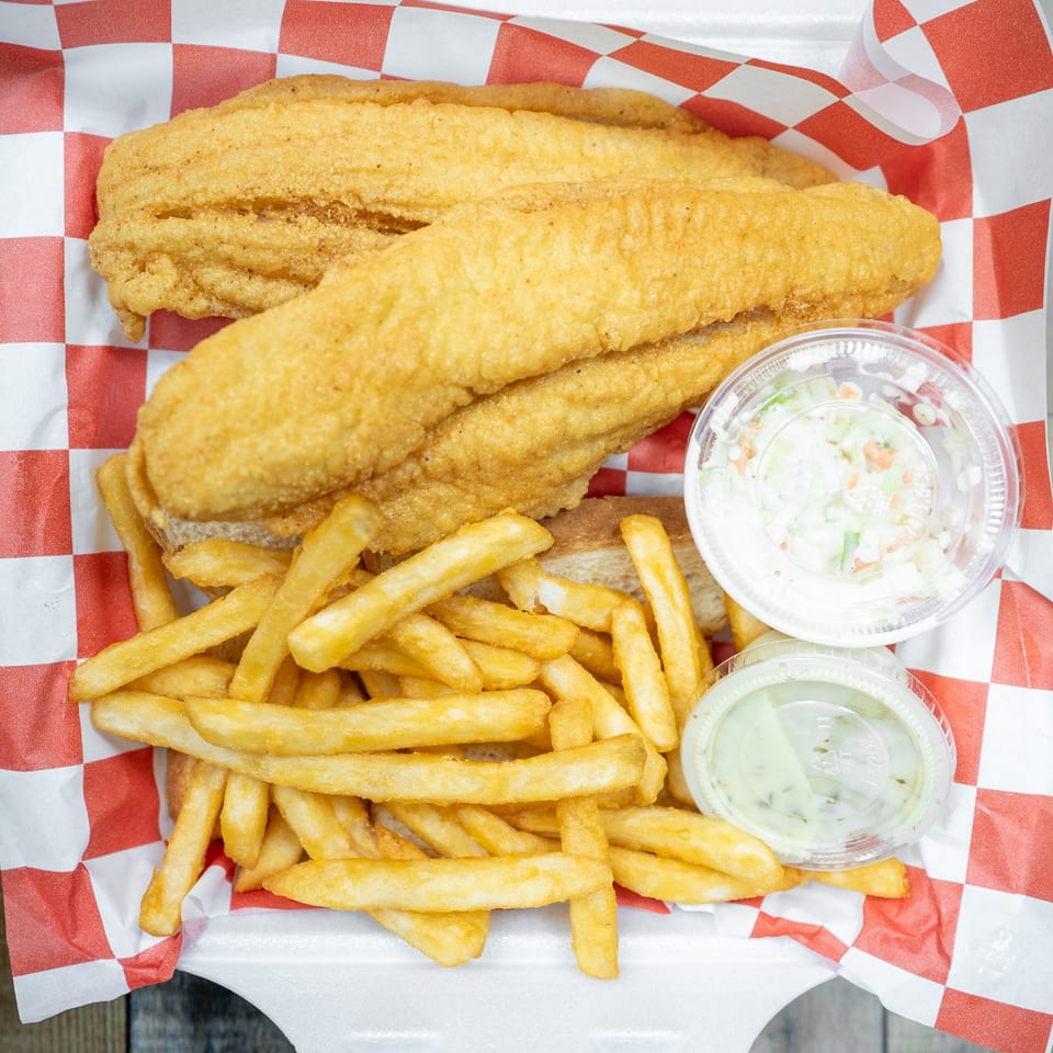 Fried fish fillets and french fries in a take-out container with coleslaw and tartar sauce.