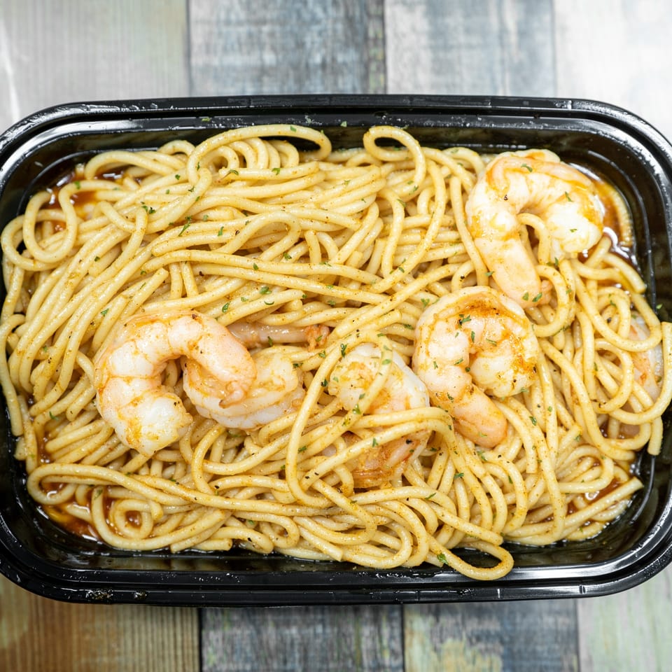 Shrimp pasta in a black container, with a light sauce and green herbs.