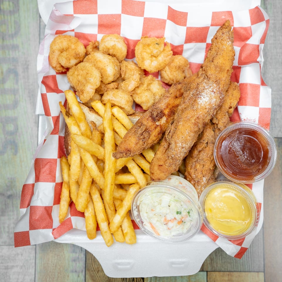 Fried fish and shrimp combo with fries, coleslaw, and dipping sauces in a takeout container.