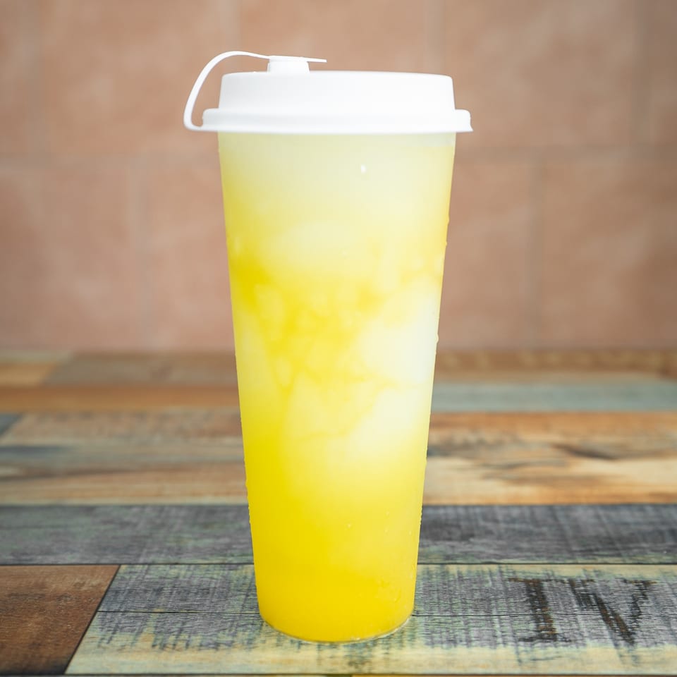 Tall plastic cup of yellow and white layered bubble tea with a white lid on a wooden table.