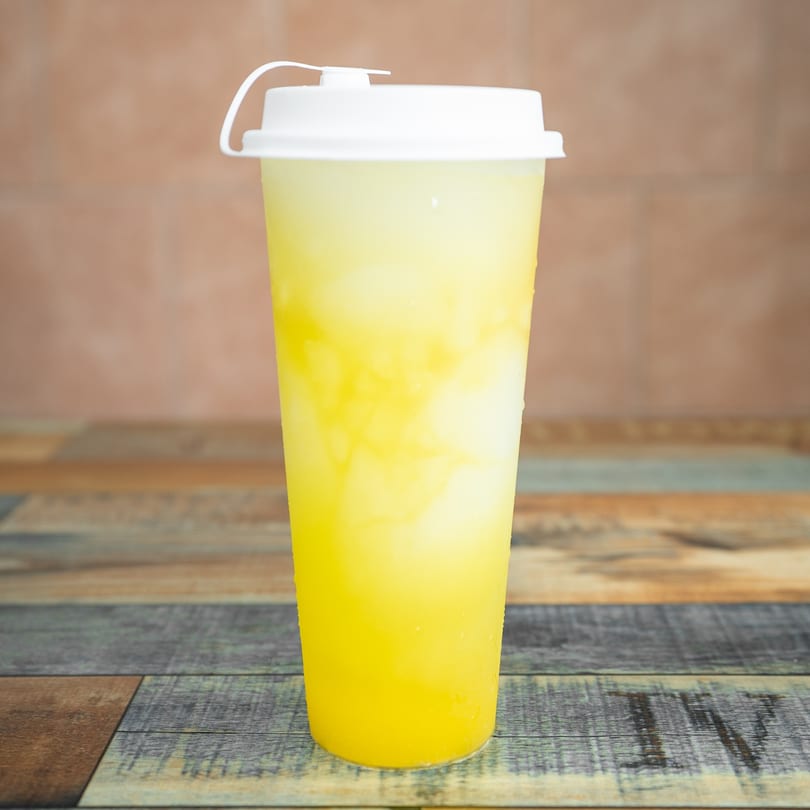 Tall plastic cup of yellow and white layered bubble tea with a white lid on a wooden table.