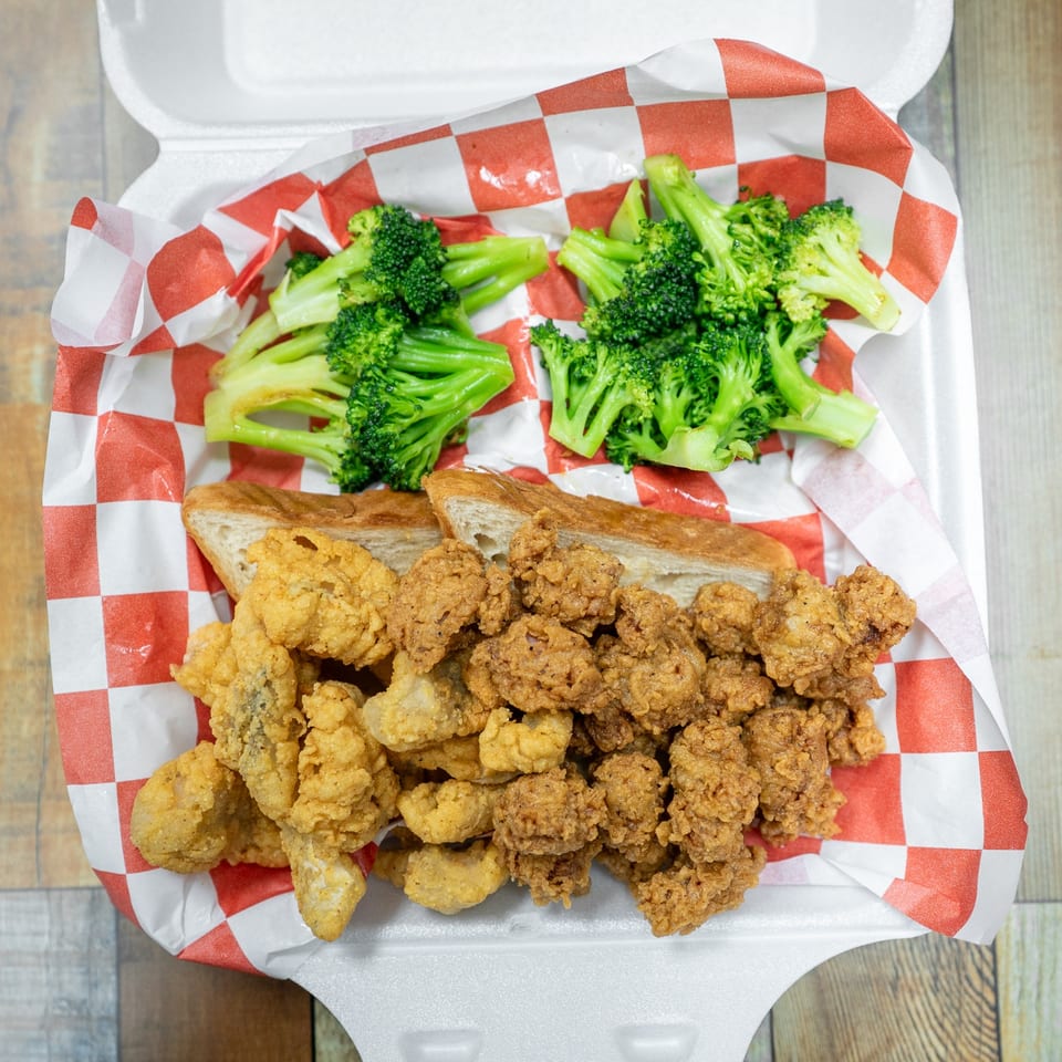 Fried seafood, broccoli, and bread in a white takeout container with red and white checkered paper.