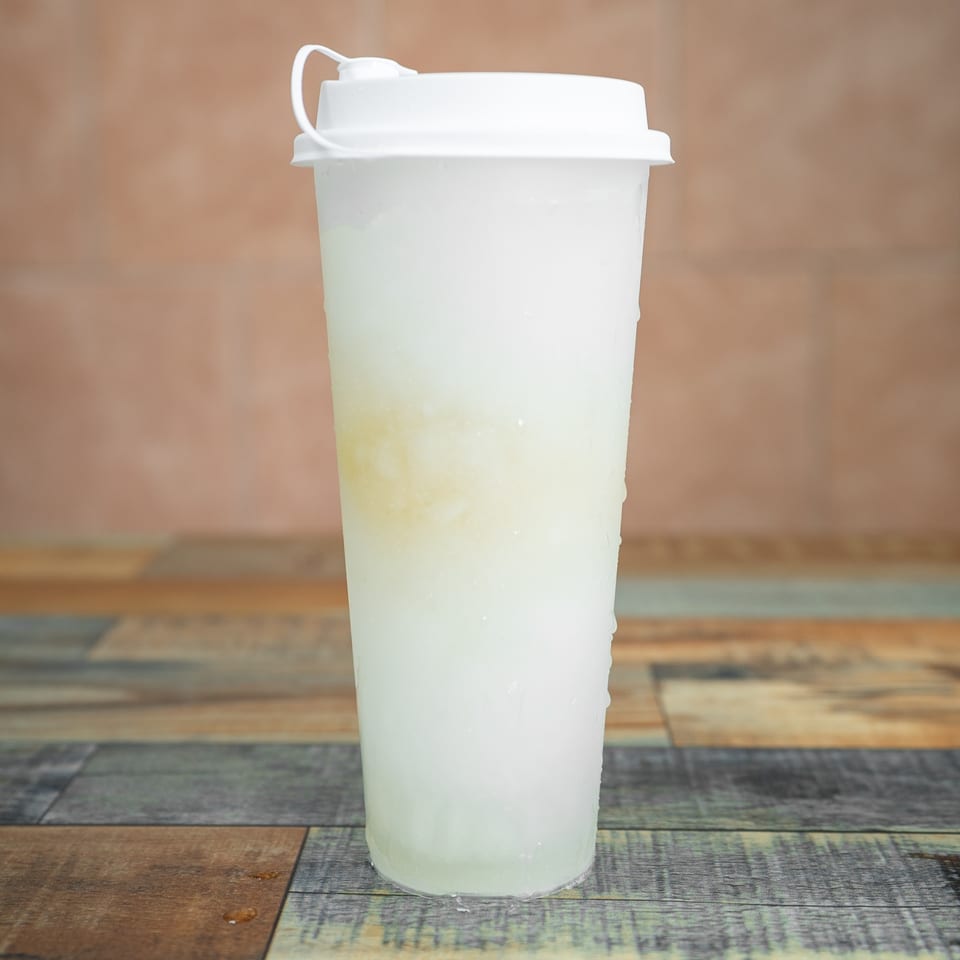 A tall, frosted plastic cup with a white lid, filled with a light-colored beverage.