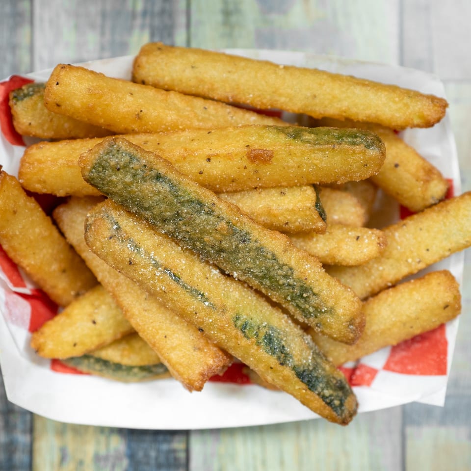 Close-up of golden-brown fried pickle spears, seasoned with salt and pepper, in a red and white checkered paper tray.